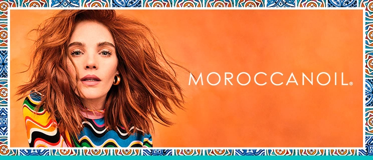 Werbebild für Moroccanoil: Eine Frau mit voluminösem, rotem Haar vor orangem Hintergrund. Sie trägt ein buntes Oberteil, eingerahmt von einer dekorativen Fliesenbordüre, die eine mediterrane Ästhetik vermittelt.